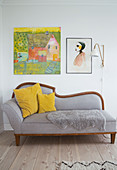 Pictures and a wall lamp above a grey day bed with cushions