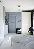 A double bed, a black chair, a white wardrobe and a chest of drawers in a blue-grey bedroom