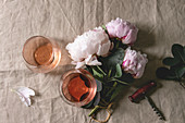 Two glasses of different rose wine standing on grey linen table cloth with pink peonies flowers