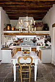 A chandelier above the dining table in a rustic open kitchen - dining room with a natural stone floor