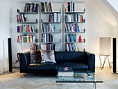 Black leather couch and glass table in front of an open wall shelf in the living room