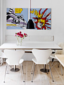 White designer chairs at a dining table under comic-style paintings