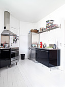 Black high-gloss kitchen with stainless steel worktop in an old building with white plank floor