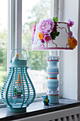 Türkisfarbene Laterne mit Gartenzwerg und Tischlampe mit verziertem Lampenschirm auf Fensterbank