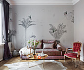 An elegant sofa in front of a wall papered with palm tree wallpaper with a coffee table and an antique chair in a living room