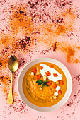 From above tasty aromatic orange vegetable cream soup with sliced carrot and parsley in white bowl on pink background