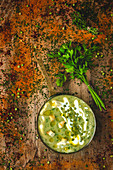 From above mashed vegetable creamy soup with small crackers, parsley and green peas on pan on wooden background