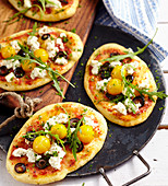 Small homemade pizzas with ricotta, olives, tomatoes and rocket