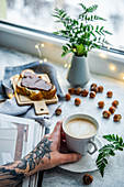 Tasse Kaffee und Brot mit Nussnougataufstrich auf winterlicher Fensterbank
