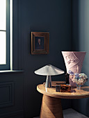 Beistelltisch mit Tischlampe und Vase in Zimmerecke, Portrait an der Wand