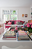 Blick über Couchtisch mit Büchern auf pink lackiertes Rattansofa mit bunten Kissen