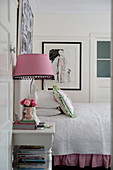 Bed with white bedspread, table lamp with gingham lampshade on bedside table and pictures on walls