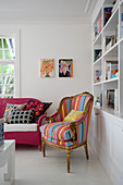 Antique armchair with striped cover and pink-painted wicker sofa next to bookcase