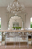 Transparent designer chairs around dining table below chandelier