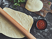 Pizza dough with a rolling pin and tomato sauce