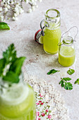 Grüner Smoothie mit Basilikum und Minze in Glasflaschen