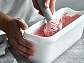 Strawberry ice cream in a container with an ice cream scoop