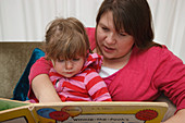 Toddler with her mum on a sofa reading a book