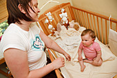 Mother putting baby into cot