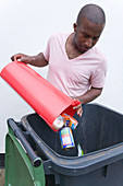 Man putting tins and cans into recycling wheelie bin