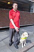 Vision impaired man and guide dog prepare to cross a road