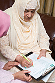 Young female carer helping older woman with form