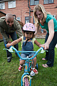 Mother and father teaching their daughter to ride a bike