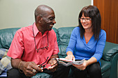 Elderly black man with carer at home looking at post