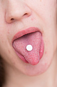 Young woman with pill on tongue