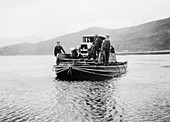 An early ferry transporting a car across a lake