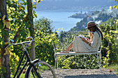 Frau mit Buch auf Bank sitzend, Blick auf See