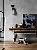 Rustic wooden table with ceramics and painting against gray wall
