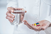 Hands with colourful pills and a glass of water