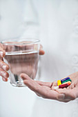 Hands with colourful pills and a glass of water