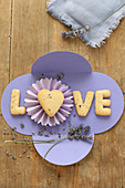 Schriftzug 'Love' aus Lavendel-Herzplätzchen auf selbstgebasteltem lila Papierumschlag