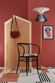 DIY-Paravent aus Wiener Geflecht, Stuhl und Stehlampe vor rot gestrichener Wand