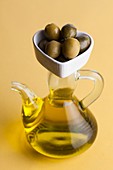 Jug of olive oil with olives in heart shaped dish