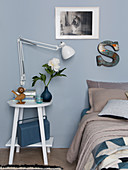Reading lamp on bedside table next to bed in bedroom with blue-grey wall