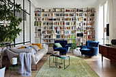 Wohnzimmer im Stilmix mit deckenhoher Bücherwand, Sofa und blauen Samtsesseln