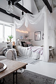 Bed with canopy in white attic room with exposed black roof beams