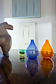 Slow design: terracotta horse and bubble vases on table with abstract artworks on wall in background