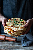 Unrecognizable man holding stack of fresh naan flatbread over lumber table in rustic kitchen