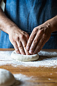 Unrecognizable male in apron flattening soft dough over table with flour while cooking pizza