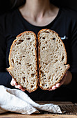 Unrecognizable person showing fresh halved bread with seeds against wooden wall