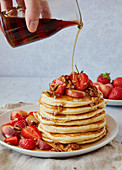 Pouring Maple Syrup Over A Stack of American Pancakes with Stawberries and Peaches
