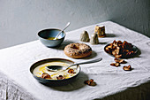Parsnip or cauliflower cream soup in ceramic bowl with butter sauce, sun dried pears, bagel bread and herbs