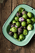 Raw Brussel sprouts in a vintage, green enamel dish, on a rustic wooden surface.