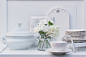 Vase of white carnations and hydrangeas and china crockery on dresser