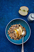 Muesli with apple wedges on a blue plate on a blue surface