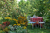 Kleiner Sitzplatz im Garten neben Staudenbeet und Apfelbaum